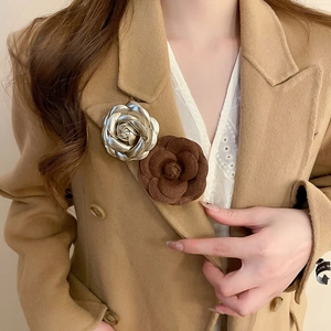 Detail of camellia flower brooches in leather and metal on a camel wool coat