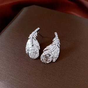 Macro view of silver feather earrings with zircon inlay on a red silk background