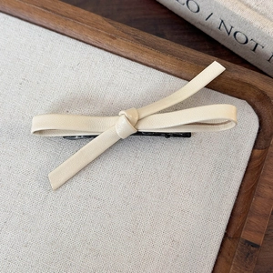 Detailed view of a creamy white leather bow hair clip on a natural linen and wood background