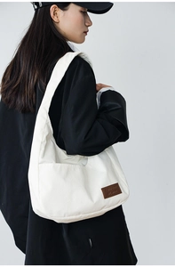 Close-up of white corduroy texture and brown leather logo tag on a minimalist shoulder bag