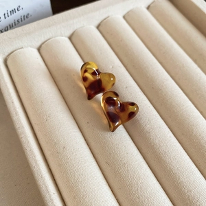 Macro shot of heart-shaped leopard resin earrings on a beige velvet jewelry tray