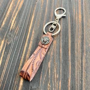 Close-up of vintage brown leather keychain with embossed patterns and turquoise stone button