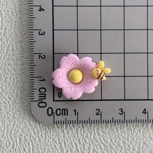 Gros plan d'une fleur rose en résine avec abeille sur une règle mesurant 2,5 cm
