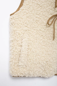Close-up of cream fleece vest featuring brown binding edges and tie closure detail
