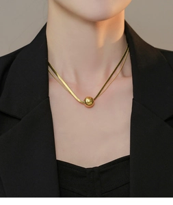 Detail of double-layer gold titanium steel necklace with polished bead on black blazer