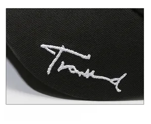 Close-up of white embroidered Trend text on black cotton twill baseball cap fabric
