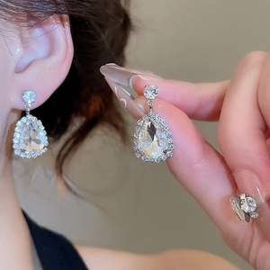 Detail view of silver teardrop earrings with crystals shown on a model and in hand