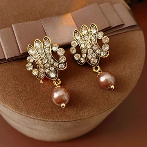 Detailed close-up of vintage golden hollow earrings with brown pearls on brown velvet