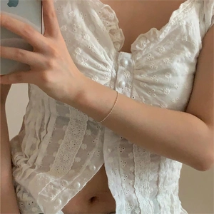 Detail of white lace crop top featuring floral embroidery and pearl button accents