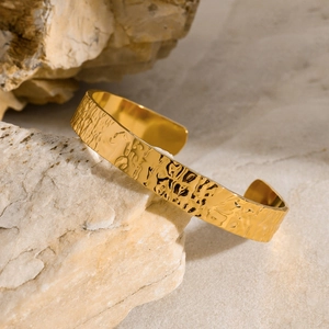 Brazalete abierto de acero inoxidable dorado con textura martillada sobre piedra natural