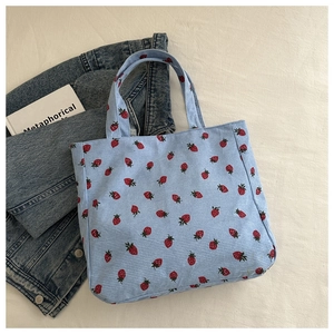 Detail van de lichtblauwe corduroy draagtas met rode aardbeienprint op denim stof