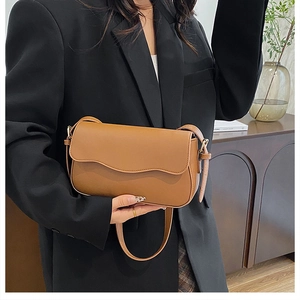 Detail of a brown leather shoulder bag with a stylish wave flap shown on a model