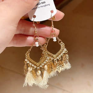 Detail of vintage gold feather earrings with beige tassels and hollow metal leaf pendants