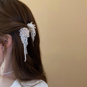 Detail of faux pearl claw clip with long tassels and pink beads on model hair