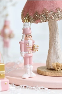 Detailed view of a pink nutcracker soldier ornament with gold gift box and glittery details