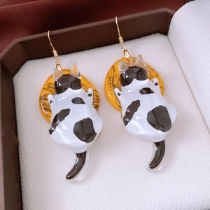 Close-up of black and white resin cat pendant earrings on yellow round base in jewelry box