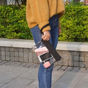Transparent PVC stadium crossbody bag with black wrist strap shown in outdoor setting