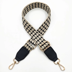 Detail of adjustable houndstooth bag strap with leather ends and gold metal buckles