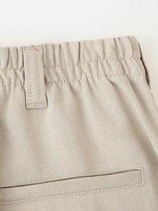 Detailed close-up of beige trousers featuring elastic waistband, belt loop and rear pocket