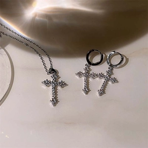 Detailed view of silver cross jewelry set with necklace and hoop earrings on marble