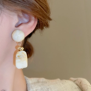 Close-up of geometric resin drop earrings with marble texture and golden metal knot detail