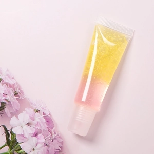 Detalle del tubo de brillo labial degradado amarillo y rosa con purpurina sobre fondo rosa