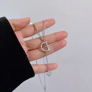 Macro detail of silver D-letter pendant and cube charm on minimalist link necklace