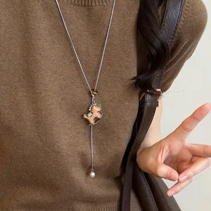 Close-up of wooden horse pendant and white pearl on a silver chain against brown knitwear