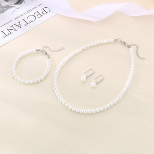 Detailed set of white pearl necklace, bracelet, and earrings on light beige fabric background