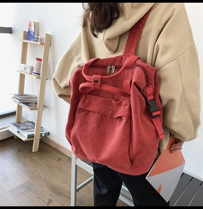 Detail of red canvas backpack with black buckle and top handles worn by a model