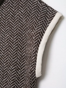 Close-up detail of herringbone knit fabric with cream ribbed edging on a brown vest