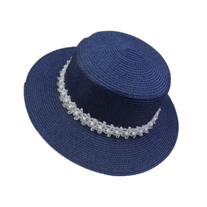Detailed view of navy blue straw hat with elegant white lace flowers and pearls