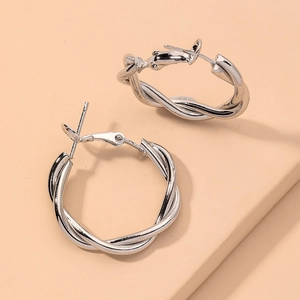 Elegant silver twisted hoop earrings with geometric design on warm textured background