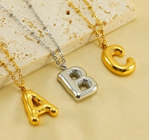 Close-up of 3D puffy gold and silver alphabet necklaces on beige stone and silk cloth