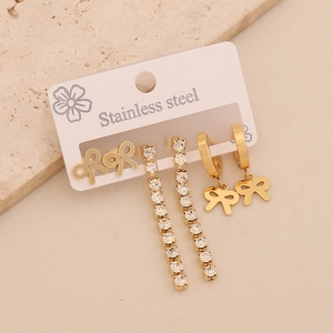 Three pairs of gold titanium steel earrings with rhinestones and bows on beige stone