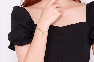 Close-up of golden adjustable heart charm bracelet on model's wrist with black dress