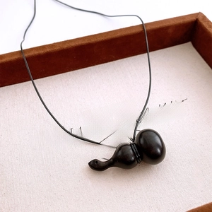 Vue macro d'un pendentif gourde en bois sombre avec un cordon en cuir noir minimaliste