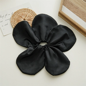 Detail of a large black flower scrunchie with satin texture on a white backdrop