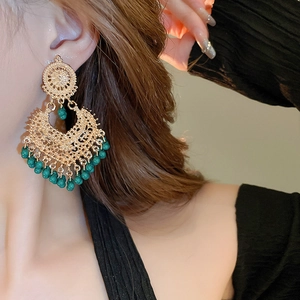 Close-up of gold hollow teardrop earrings with green beads on a female model