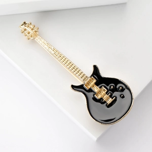 Close-up detail of a black and gold guitar brooch with fine enamel finish on white base
