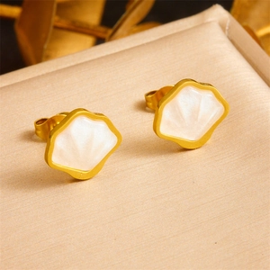 Elegant gold shell stud earrings with white pearl texture inlay on beige fabric