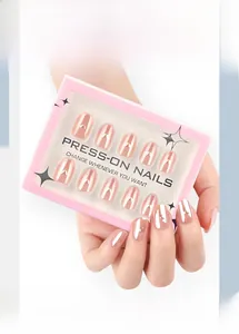 Close-up of nude pink almond press-on nails with gold heart accents in hand-held display