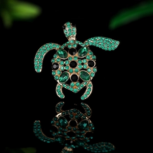 Elegant gold-tone sea turtle brooch with green rhinestones on a reflective surface