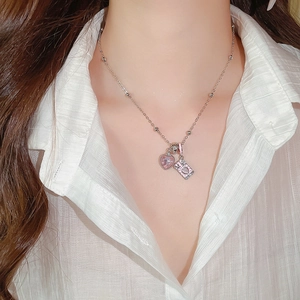Detail view of a silver-tone necklace with pink heart and envelope pendants on a model