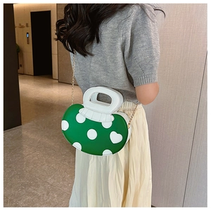 Detail of green polka dot handbag with white handle and golden chain strap on model