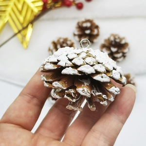 Close-up of hand holding a natural pine cone with white snow effect and metal ring hook