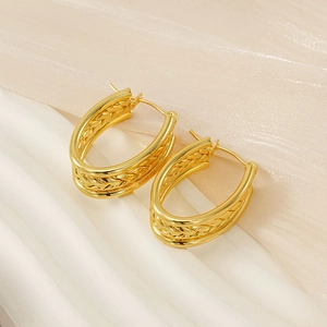 Macro shot of gold oval hoop earrings with twisted woven texture on soft fabric