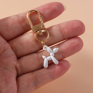 Close-up of a white balloon dog keychain with a gold metal clasp held in hand