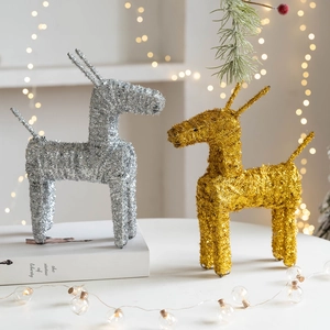 Golden and silver Christmas reindeer ornaments with glitter on table with warm lights