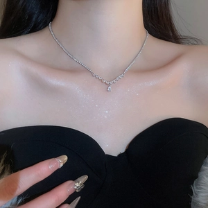 Detail of elegant V-shaped silver necklace with teardrop zircon pendant on female neck